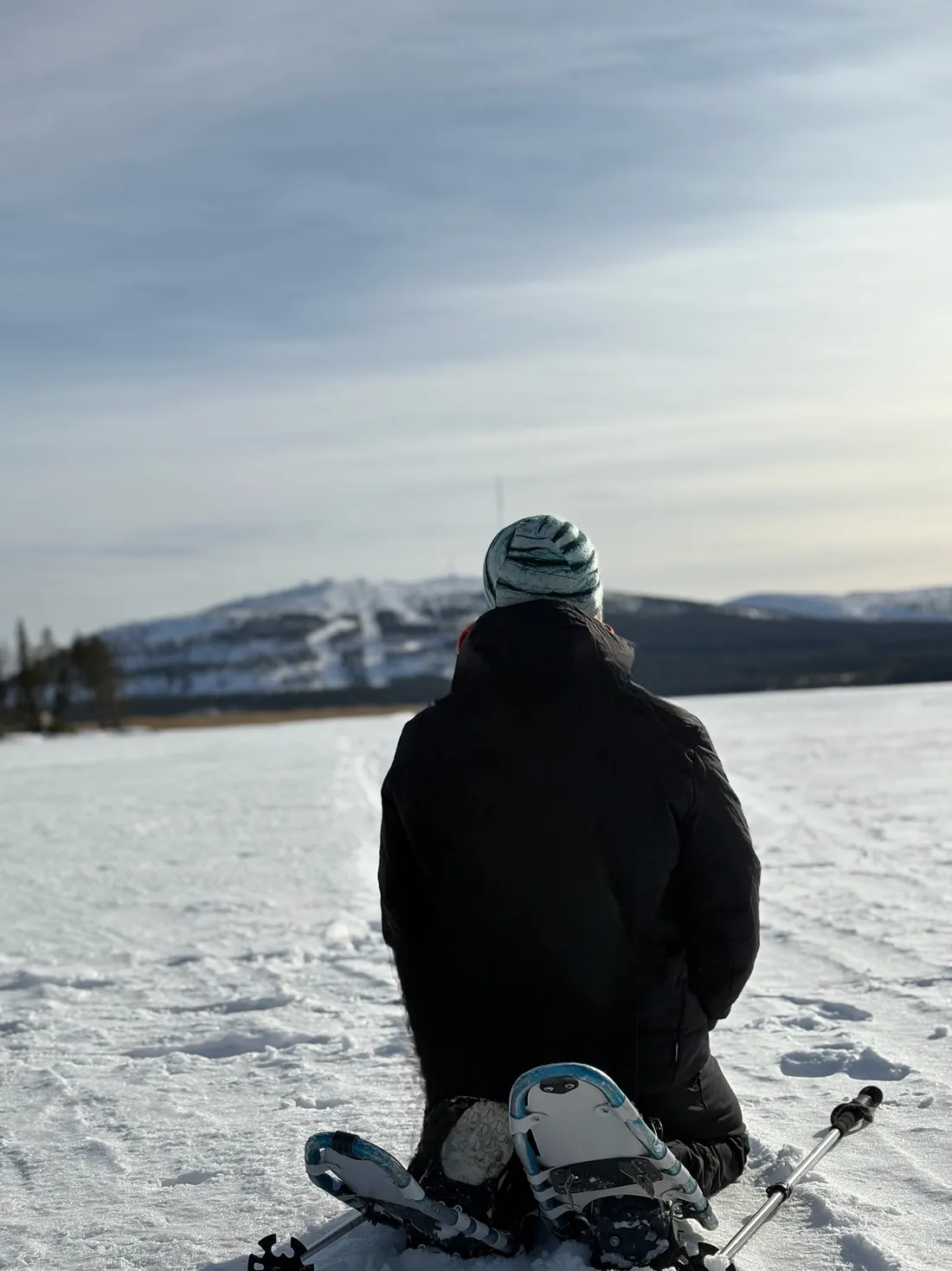 Robert Mittl kniet mit Schneeschuhen auf einem zugefrorenen See in Lappland und blickt zu den Bergen